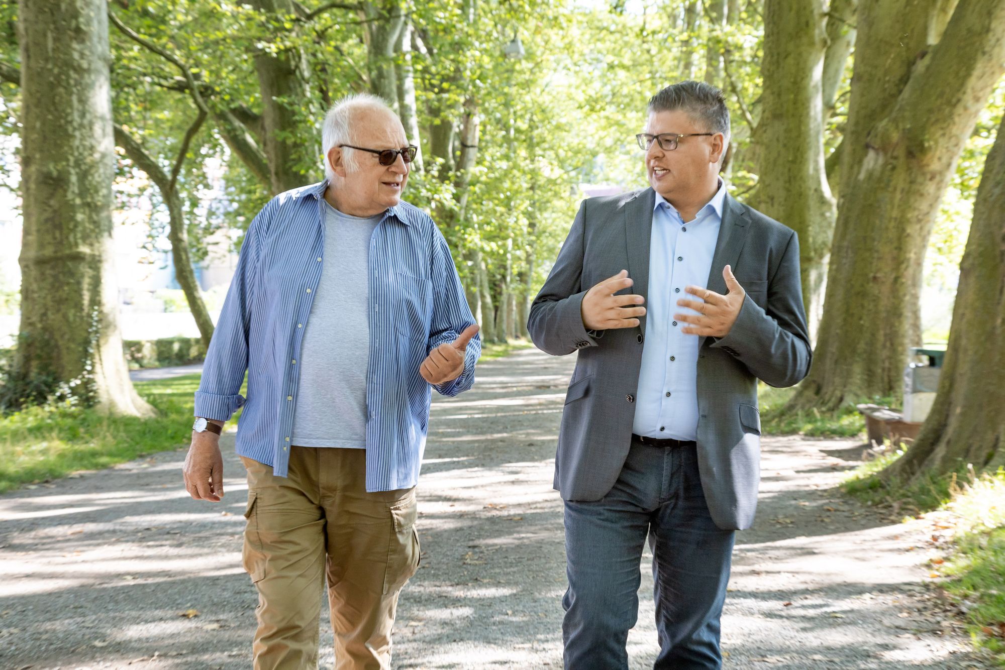 Daniel Lede Abal gehend im Gespräch mit einem älteren Mann auf der Tübinger Platanenallee auf der Neckarinsel