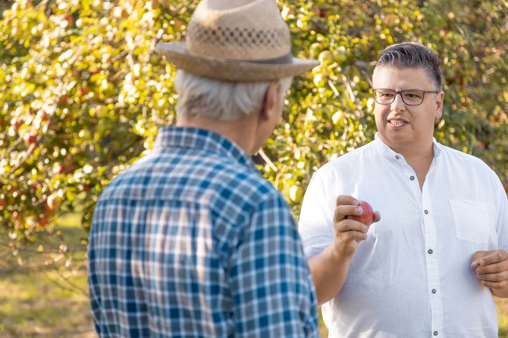 Daniel Lede Abal hält einen Apfel in seiner rechten Hand umschlossen im Gespräch mit einem älteren Mann auf einer Streuobstwiese in Mössingen